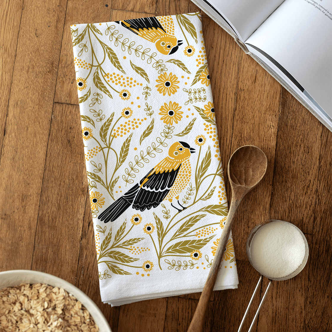 Floral towel with bird design on a wooden surface with kitchen items.