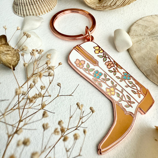 Decorative keychain shaped like a cowboy boot with floral patterns on a light surface with natural elements.