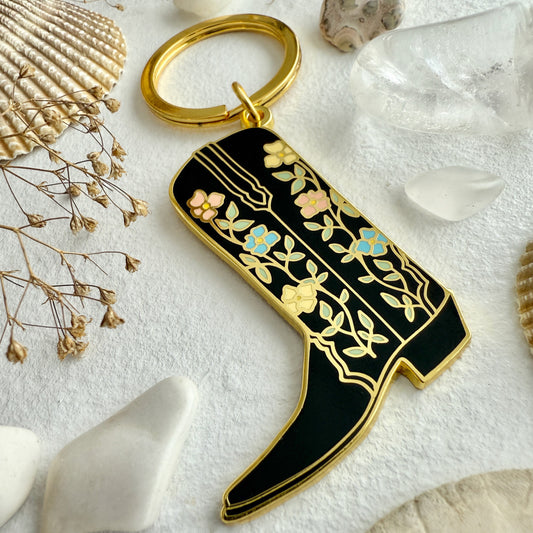 Decorative keychain with floral design on a textured surface with shells and dried flowers.