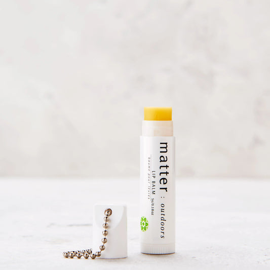 A stick of lip balm with a white label and yellow cap, placed next to a keychain on a light background.